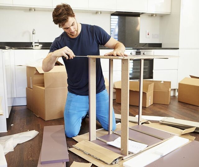 Man Putting Together Self Assembly Furniture In New Home On Both Knees
